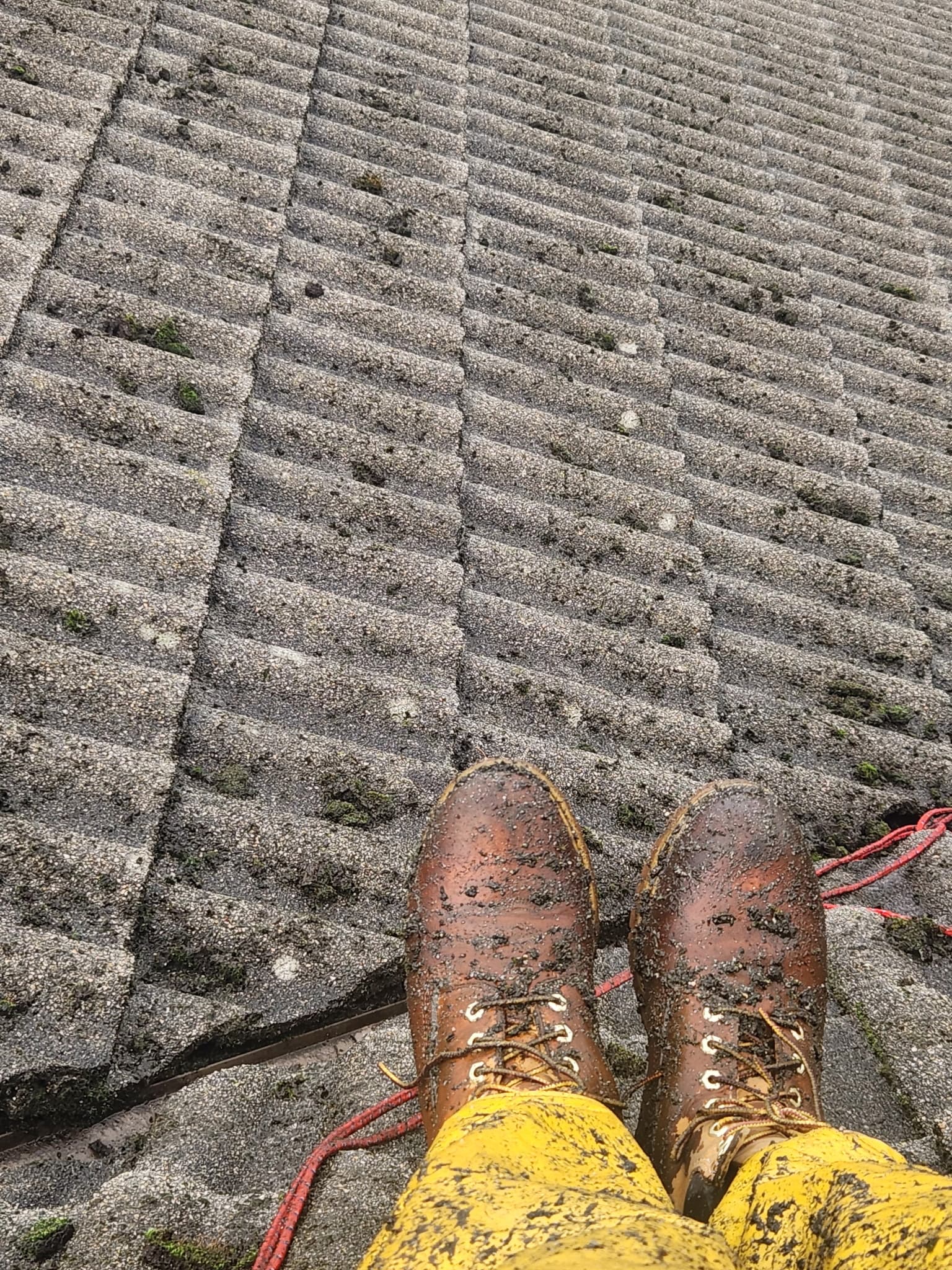 Muddy brown boots and yellow pants on a textured grey corrugated roof with rope.