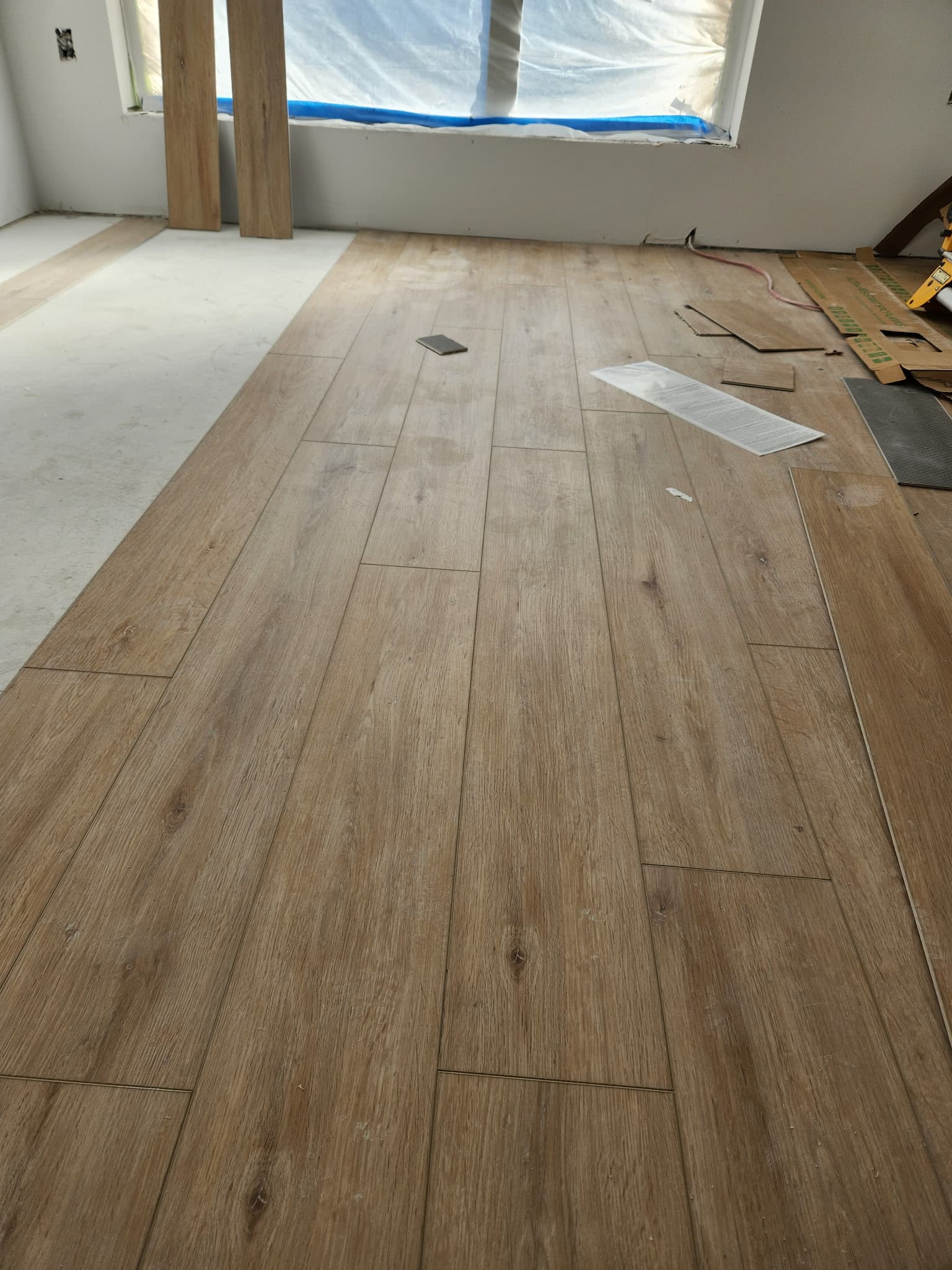 Light brown wood-look plank flooring being installed in a room under renovation with white walls.