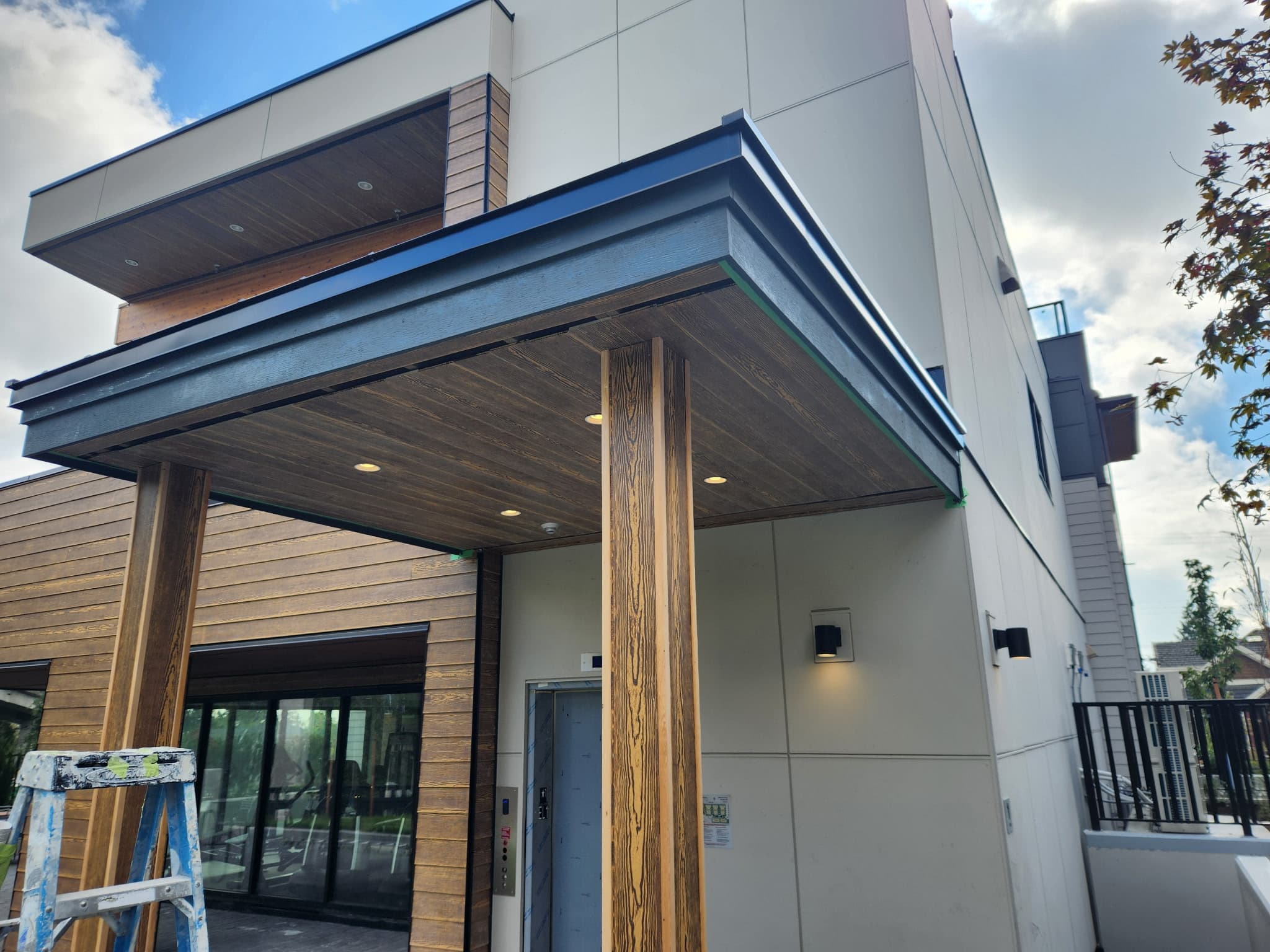 Modern building entrance with a dark wood canopy, recessed lighting, and a wooden pillar.
