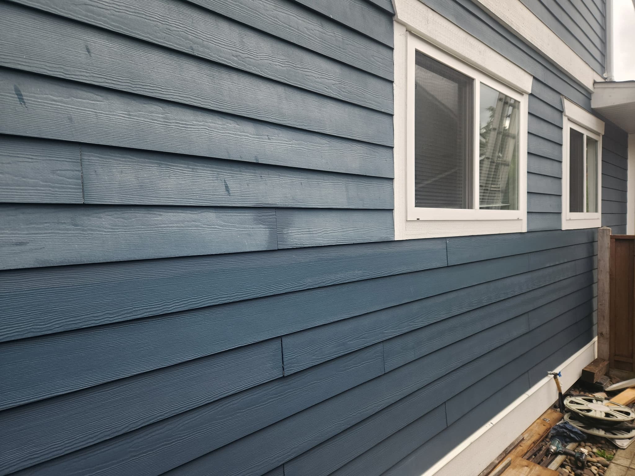 Side view of a house with blue horizontal lap siding and two white-trimmed windows.