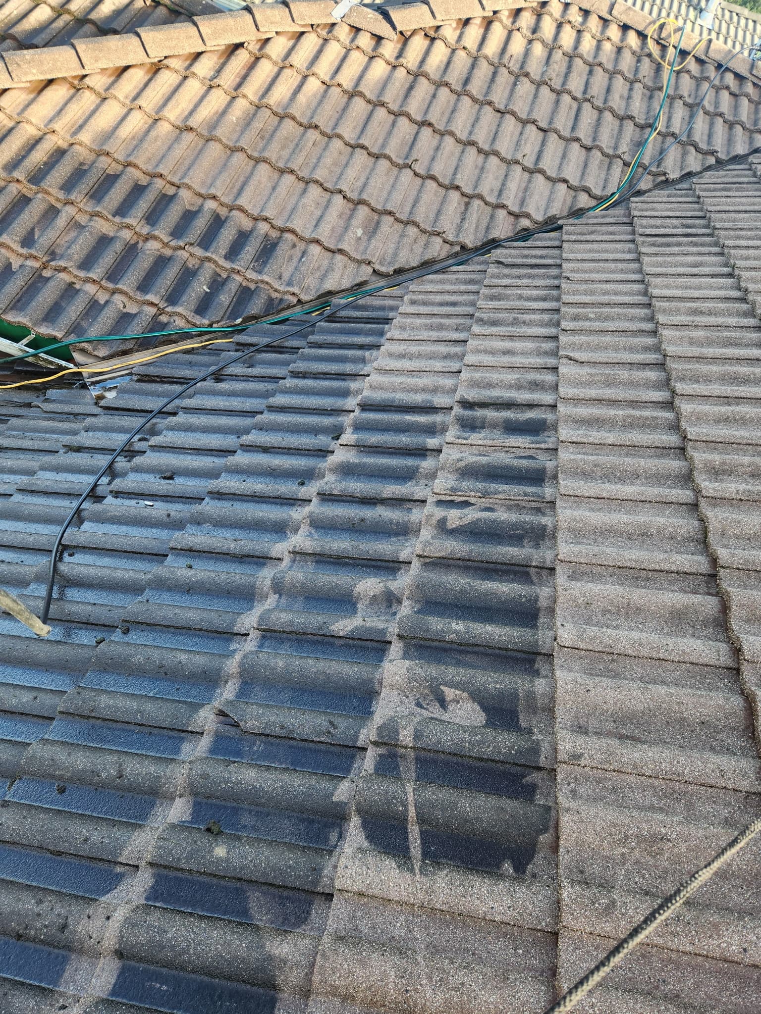 Weathered concrete tile roof with dark wet patches and electrical wires running across the surface.