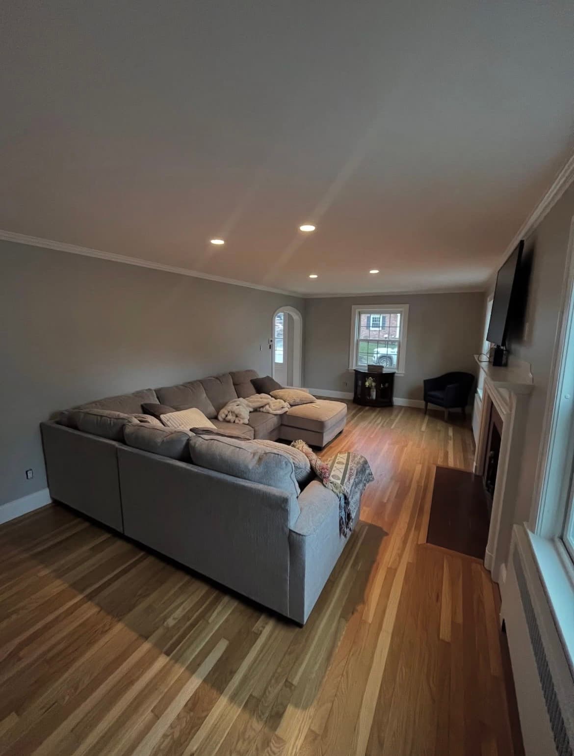Spacious living room with a grey sectional sofa, hardwood floors, and a white fireplace mantel.